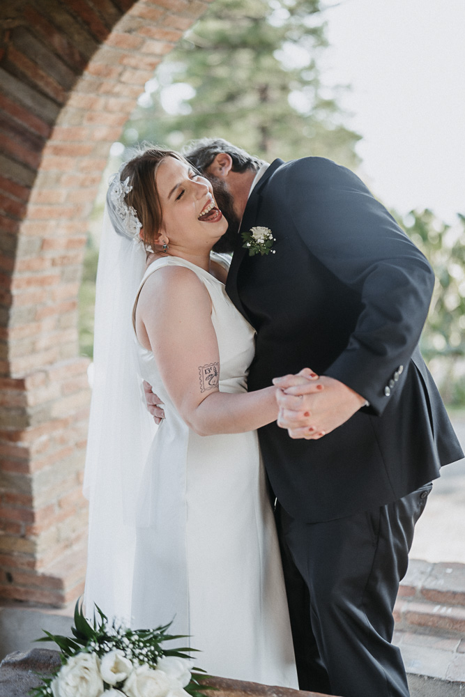 The bride laughs during the photoshoot, the groom kiss her in the neck, taormina Sicily